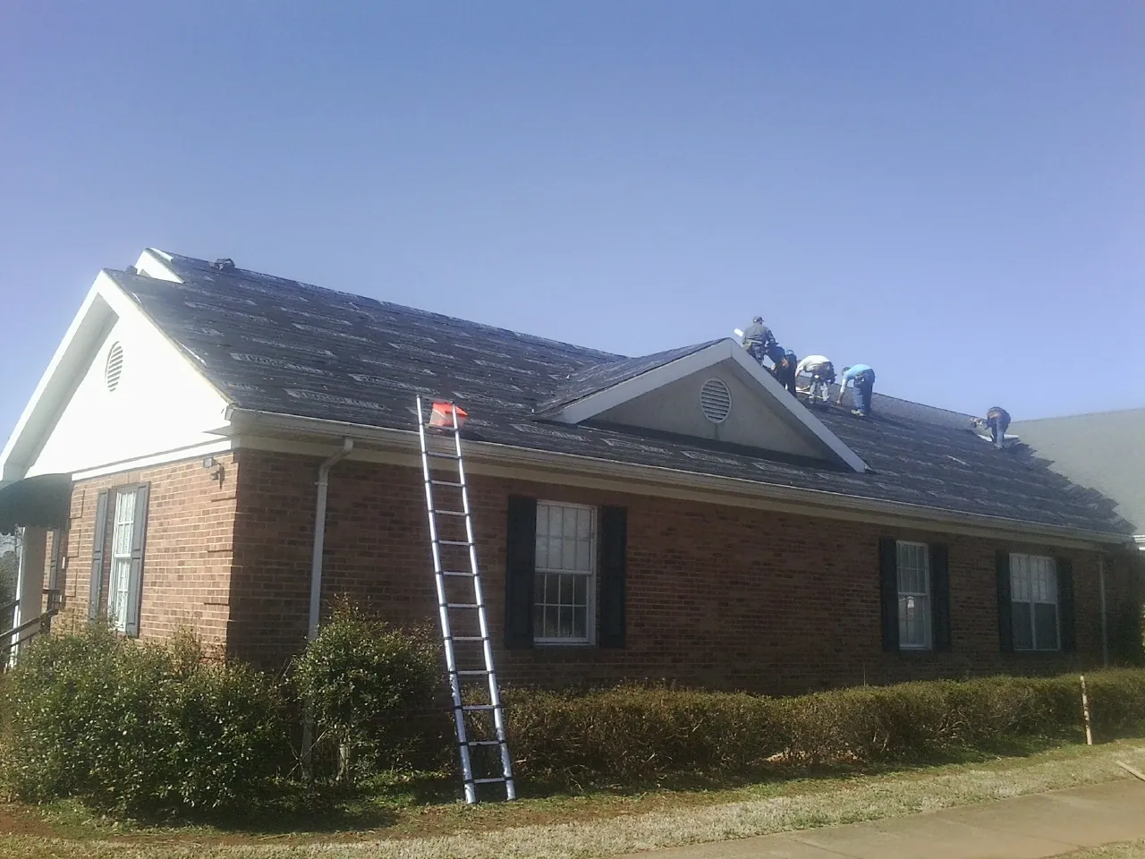 Crew tearing shingles off a brick ranch roof with a ladder set — Metal Roof Repair work by our crew in North Grosvenordale