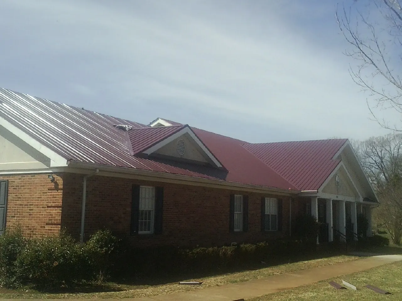 Red metal roof with gabled entries on a long brick building, from a Hail Damage Roof Repair job in North Grosvenordale