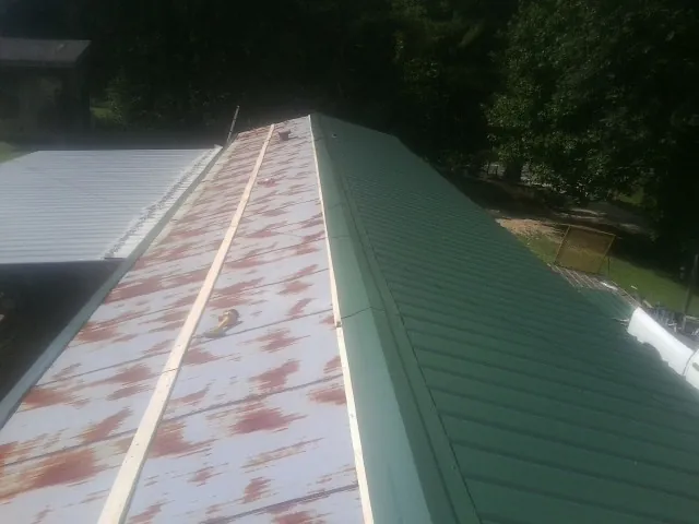 Old rusted panels beside newly installed green metal roofing — Wind Damage Roof Repair by Roofing Brothers in North Grosvenordale