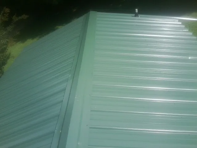 New green metal panels meeting at the ridge of a roof — Flat Roof Repair work by our crew in North Grosvenordale