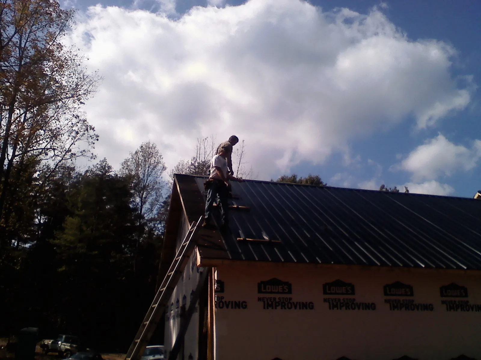 Roofer fastening dark metal panels high against a cloudy sky, from a Roof Inspection job in North Grosvenordale