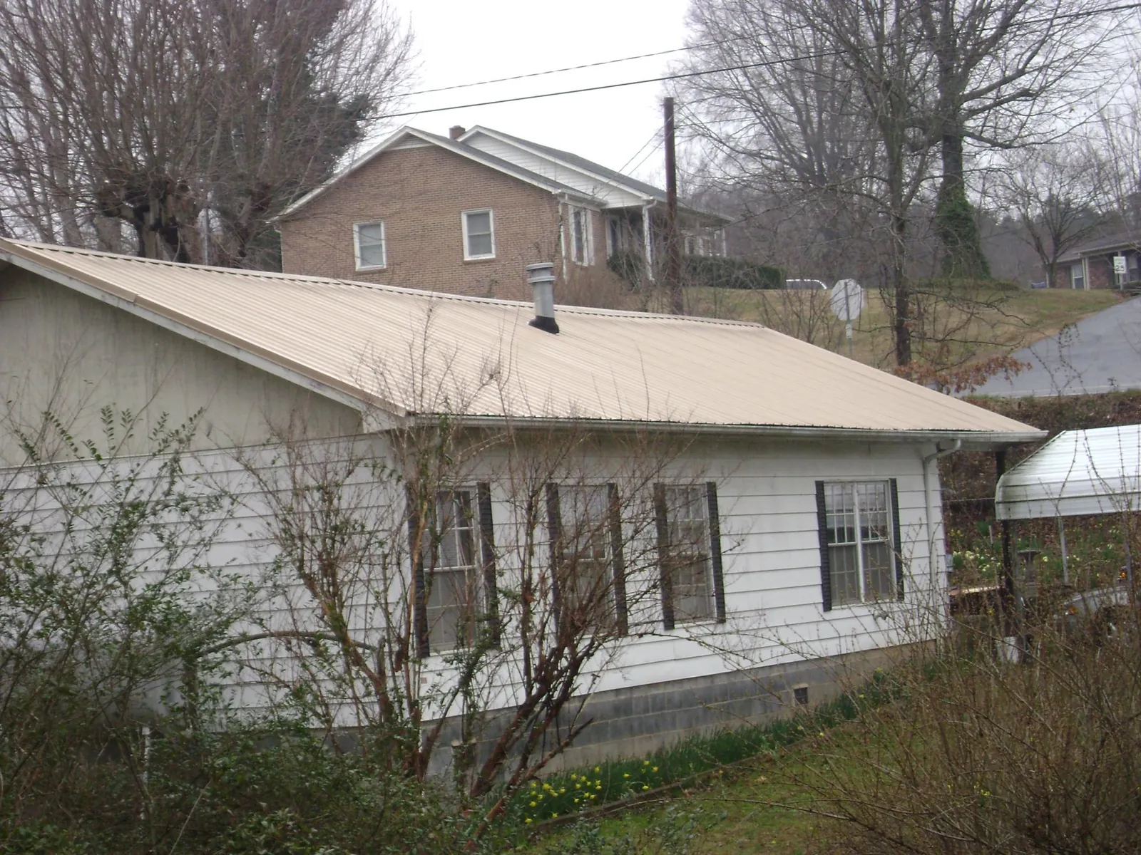 Tan metal roof on a white sided house set into a hillside — Commercial Roofing by Roofing Brothers in North Grosvenordale